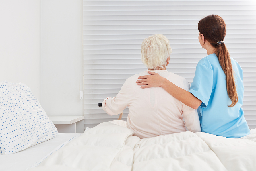 Female nurse helps senior woman out of bed
